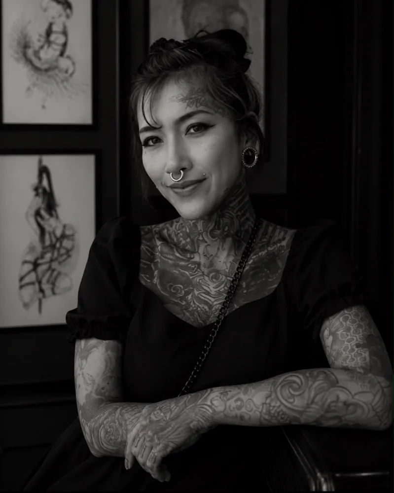 Gwen, female tattoo artist in Pattaya, seated in front of her framed drawings