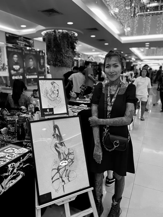 Gwen, female tattoo artist in Pattaya, beside her framed drawings at an exhibition