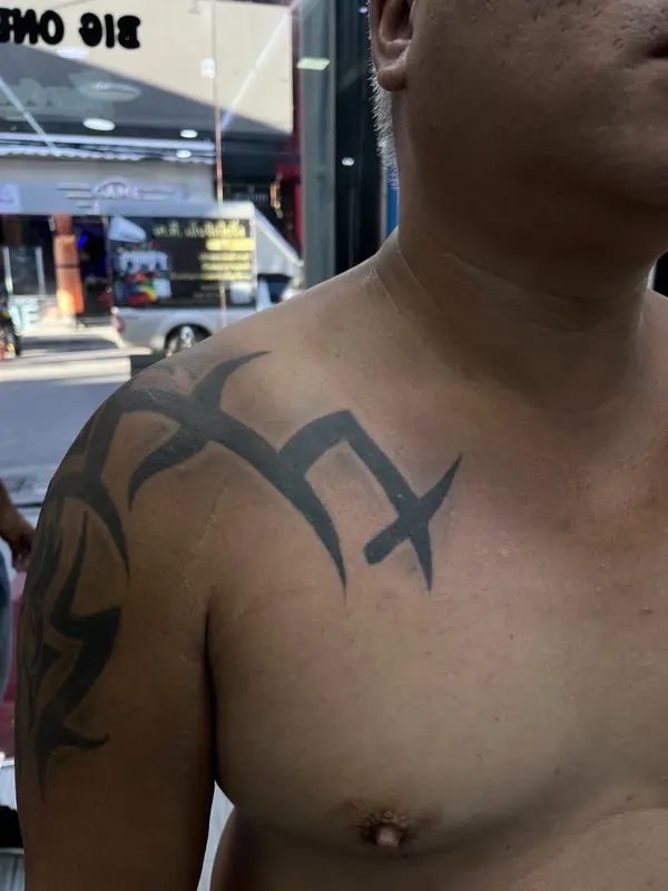 Before: solid black tribal tattoo on the shoulder and chest, before a cover-up by Gwen in Pattaya